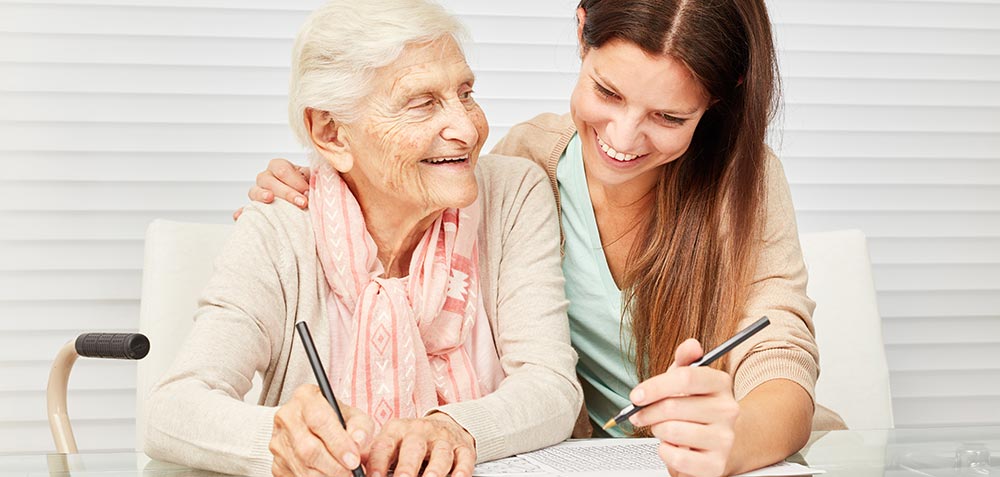 Senior Woman Writing With Caregiver