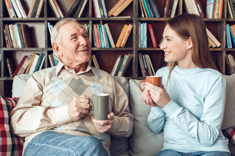 Old man and caregiver sitting on couch talking