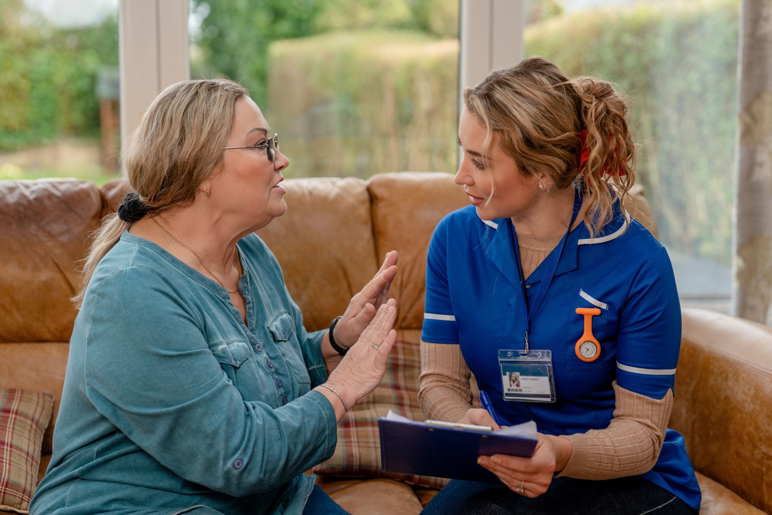 An at-home caregiver speaks to a woman about a senior's healthcare plan.