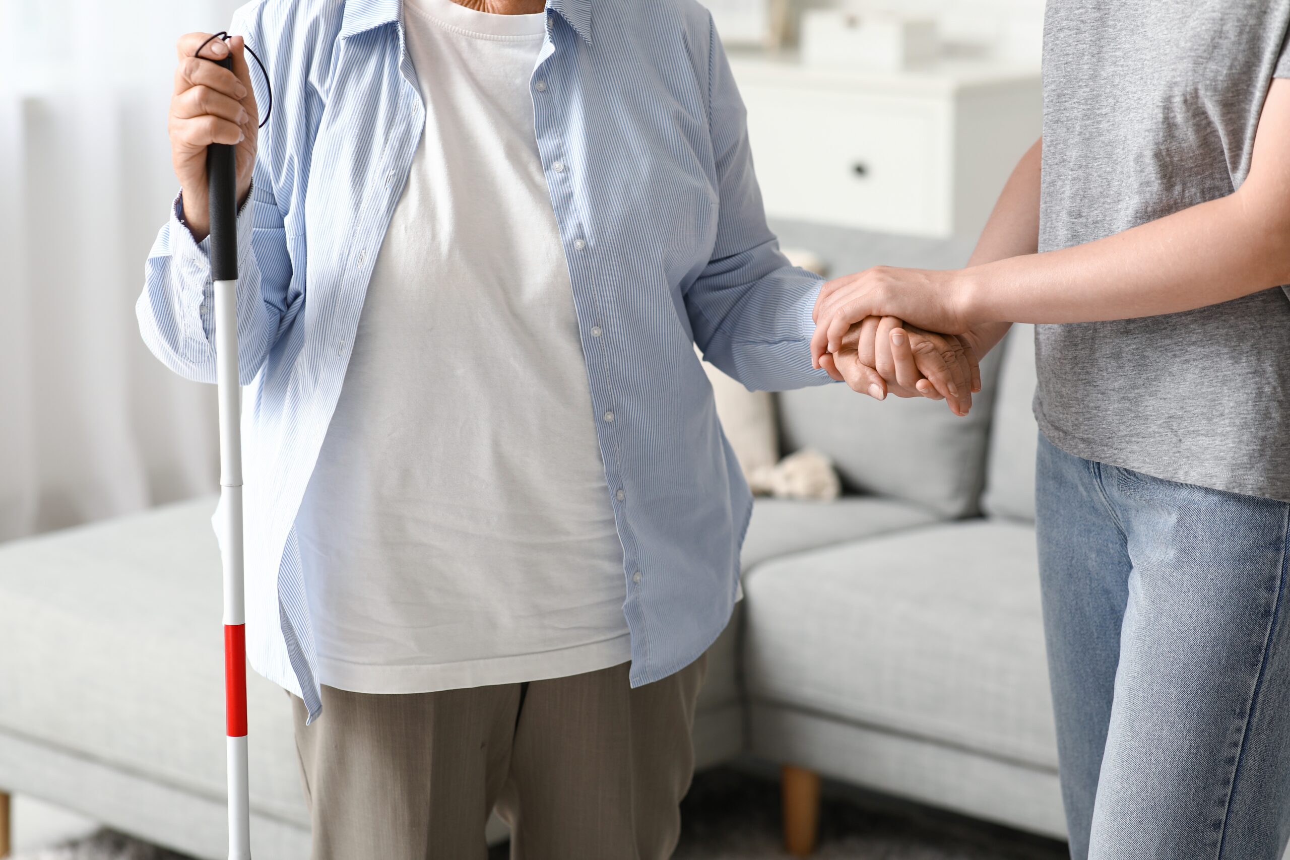 A woman assists a blind elderly woman navigate her home safely.