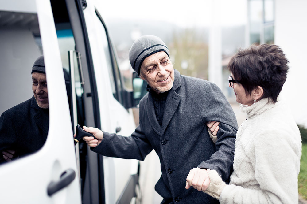 woman helping elderly man into van