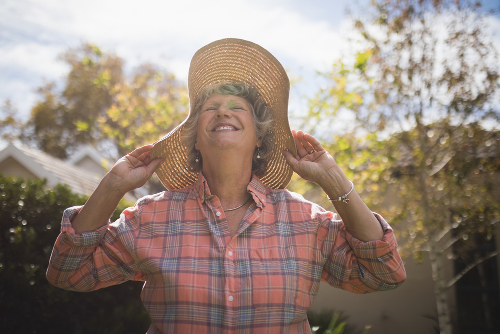 Senior woman outside in the sun wearing a big sun hat.