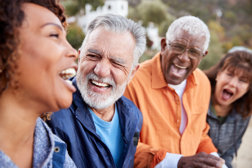Quatre personnes âgées alignées dehors rient et sourient. 