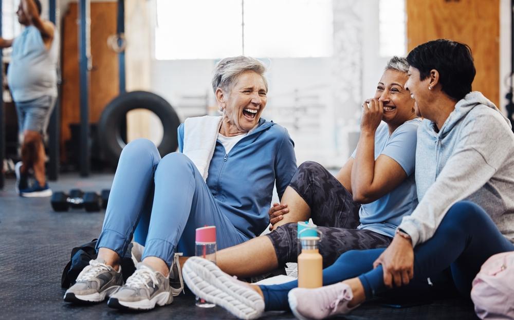 Three senior citizens exercising on the floor laughing and having a good time.